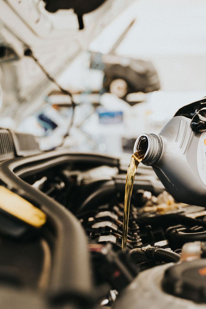 Close-up of a mechanic pouring engine oil into a car engine in an auto repair shop.